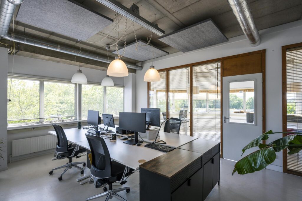 Modern kantoorinterieur aan de Anthony Fokkerweg met bureaus, computerschermen en grote ramen met uitzicht op groen.